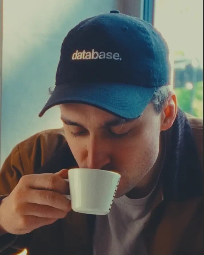 Person drinking coffee wearing a database cap